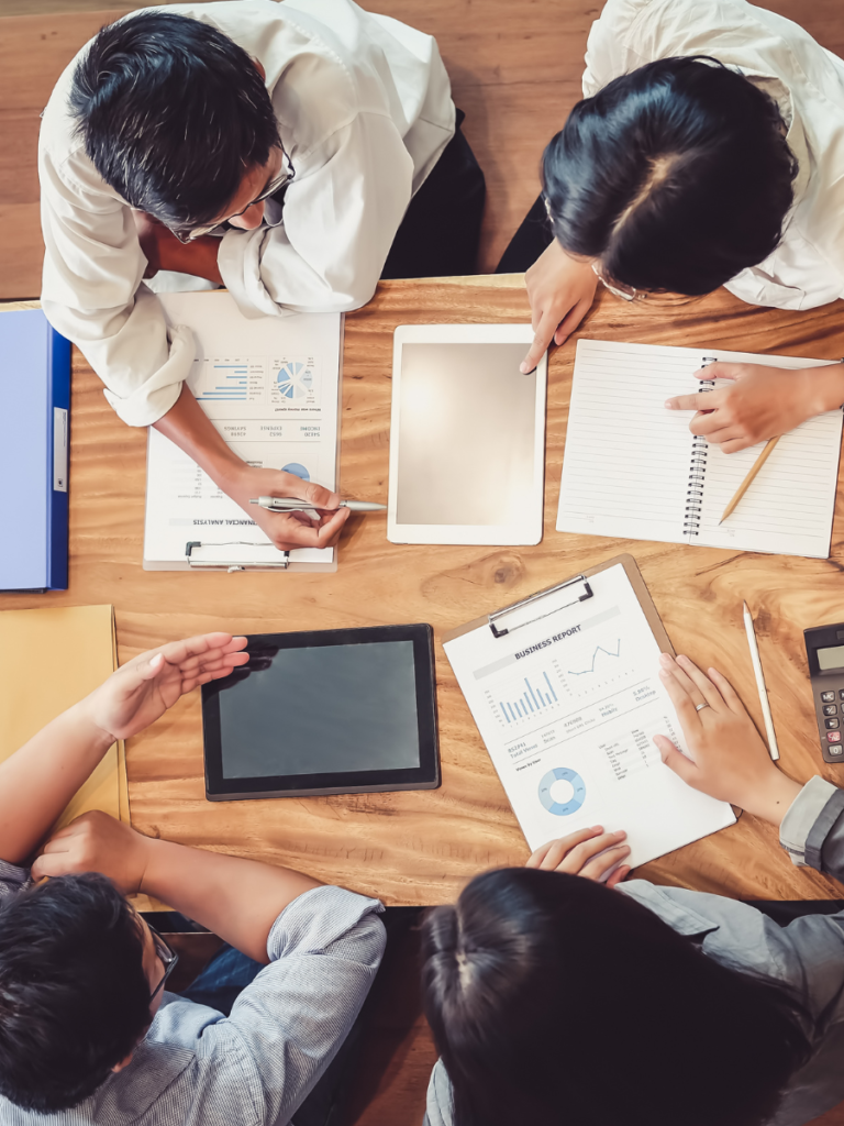 4 personas trabajando en torno de una tablet y de hojas de papel